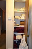 Photo showing shelf with stacks of folded linens in various colors inside closet, including white and maroon towels and linens.