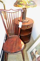 Side view of vintage wooden chair positioned next to the round wooden lamp table with a stained glass-style lamp on top