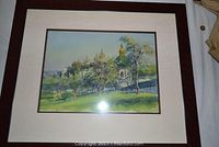 Framed watercolor painting showing a nature scene with trees, architectural elements, and a scenic background under glass with dark frame and white matting.