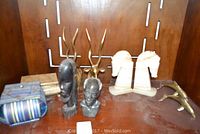 View of all decorative items together showing brass impala heads, onyx horse head bookends, stone busts, wooden tribal mask, and decorative boxes.