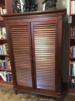 Front view of a tall wooden entertainment cabinet with two louvered doors and a dark brown finish.