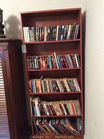 Five-shelf wooden bookcase filled with books of various sizes and cover types viewed from the front