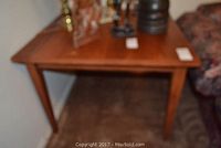 Square hardwood table in a corner showing top and legs, medium brown color, smooth finish