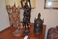 Photo showing three carved wood art pieces including the multi-armed figure, abstract sculpture, and head bust, displayed on a table.