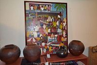 Frontal view showing framed colorful original oil painting of an African market scene and three round South African art pots placed on wooden surfaces.