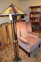 Full view of Tiffany style floor lamp and wingback chair together in a living room setting.