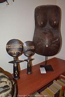 Three wooden fertility sculptures, including a large mounted woman's torso on the right and two smaller stylized figures on the left, showing front view and placement together.