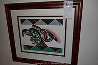 Front view of framed lithograph with stylized bird head in red, green and black on a beige double mat and dark wood burl frame