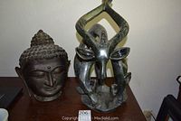 Two sculptures placed on a wooden surface: an iron Buddha bust on the left and a green stone giraffe sculpture on the right.