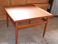Full view of vintage teak table showing the square top and four legs with horizontal supports, set on tiled floor under natural light.