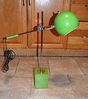 Full view of the green adjustable lamp showing square block base, vertical chrome pole, adjustable arm, dome shade and power cord.