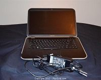 Laptop open with screen off, shows keyboard and charger in front.