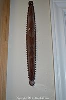 Front view of the long wooden carved mask with geometric patterns and shell inlay on eyes, hanging on wall.
