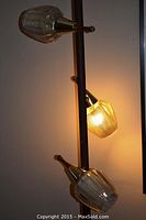 Mid-century modern vintage tension pole lamp with three lit glass shades mounted on wooden arms with metal lattice diffusers.