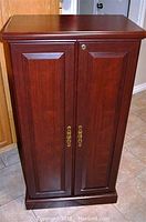 Full frontal image of the wooden storage cabinet showing two paneled doors with brass handles and locking mechanism at top right.