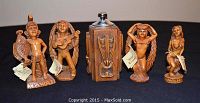 Photo showing 4 hand-carved CoCo Joe's Hawaiian figures and one wooden table lighter with carved tiki designs arranged in a row.