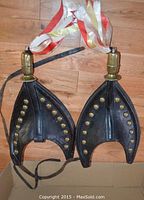 Photo showing both black leather Scotch tops with brass studs and tassels, displayed flat on wooden floor.