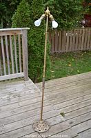 Full view of the vintage brass double outlet floor lamp standing on a wooden deck, showing height and overall condition.