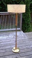 Full view of the vintage torchiere floor lamp standing on a wooden deck, showing the round metal base with wooden accents and fabric shade.