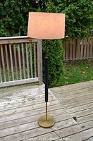 Full view of the vintage metal torchiere floor lamp showing its height, round brass base, black wooden accent on the pole, and beige fabric shade.