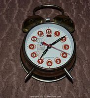 Front view of vintage brass-colored two-bell manual wind-up alarm clock with Pillsbury Dough Boy on dial