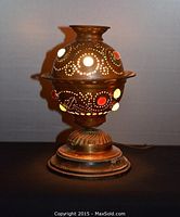 Vintage brass desk lamp with a perforated dome and colorful plastic jewels placed on a dark surface; one jewel missing, showing lamp design and condition.