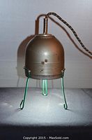 Photo of steampunk style string light showing metal shade, ridged detail, three wire legs, and cloth covered cord.