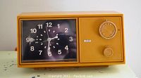 Close-up image of vintage RCA orange clock radio showing black clock face with white numerals, tuning dial, and volume knob.