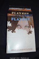 Photo showing the front covers of the ten vintage Playboy magazines stacked with the top magazine showing a partial puzzle piece design and a woman's eyes.