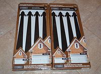 Two unopened boxes of Everbilt decorative garage door hinge kits lying flat on floor, each containing four black fleur-de-lis style hinge straps.