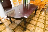 View of the dark brown solid wood table showing its top surface, turned legs, and overall condition with chips and wear.