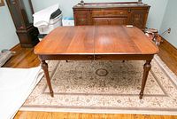 Front view of the vintage rectangular wooden dining table on a patterned rug, showing medium-dark wood finish and turned legs.
