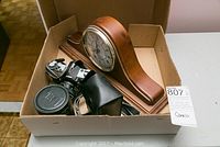 Box containing Canon AE-1 camera, leather case, lenses, flash, and wooden mantel clock.