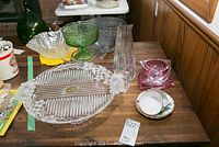 Display of assorted glassware including clear and colored pieces, teacups and ashtrays on wooden table