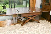 Wooden expandable coffee table with the top folded in half, showing the X-shape crossed leg base and slatted wooden top panels.