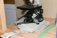 Left angled view of microscope showing base, stage, and wired illumination system placed on a wooden surface.