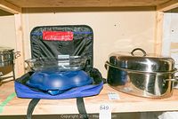 Photo showing an oval metal roasting pan with lid beside a blue insulated carrying case containing a clear glass casserole dish and a blue cold pack container.