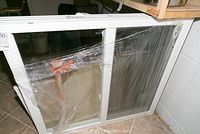 Double slider window wrapped in clear plastic, leaning against shelving and wall.