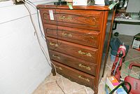 Frontal view of the wooden chest of drawers showing five drawers with brass handles and wood grain detailing.