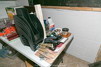 Photo of black plastic file folders, staplers, and electric pencil sharpener on a table along with other office supplies items.