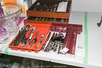 Various stainless steel knives, forks, and spoons laid out in trays and boxes on a table.
