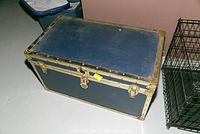 Blue trunk with gold metal trim, lock with key, and side handles viewed from above.