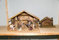Full view of wooden nativity scene with stable and figurines including Mary, Joseph, baby Jesus, wise men, angels, and animals on a shelf.