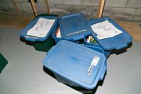 Six large plastic bins with lids labeled 'Poetry Books', 'Primary Books', and others, containing books and educational materials.