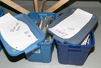 3 blue plastic bins on floor labeled 'Books with tapes' and 'Legos' containing items in lot.