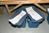 Two blue plastic bins labeled 'Cook Books' and 'Meditation Books' placed under wooden shelving