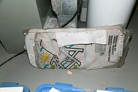 Cushion wrapped in clear plastic showing sun and chair graphic design, partially covered by paper label.