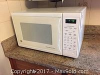 Front view of white GE microwave oven on countertop, showing closed door and digital control panel on right side.