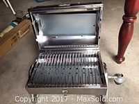 Photo showing grill open with visible stainless steel grilling surface and propane tank connection.