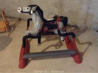 Full view from the side showing the gray horse on the red and black metal frame with cushion roller.